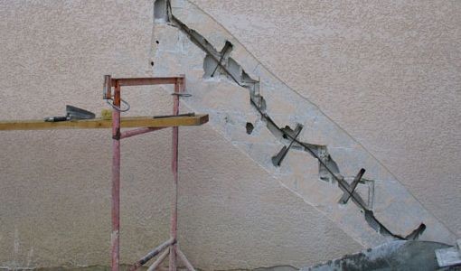 Wall with diagonal crack and visible reinforcements, next to a wooden scaffolding frame.