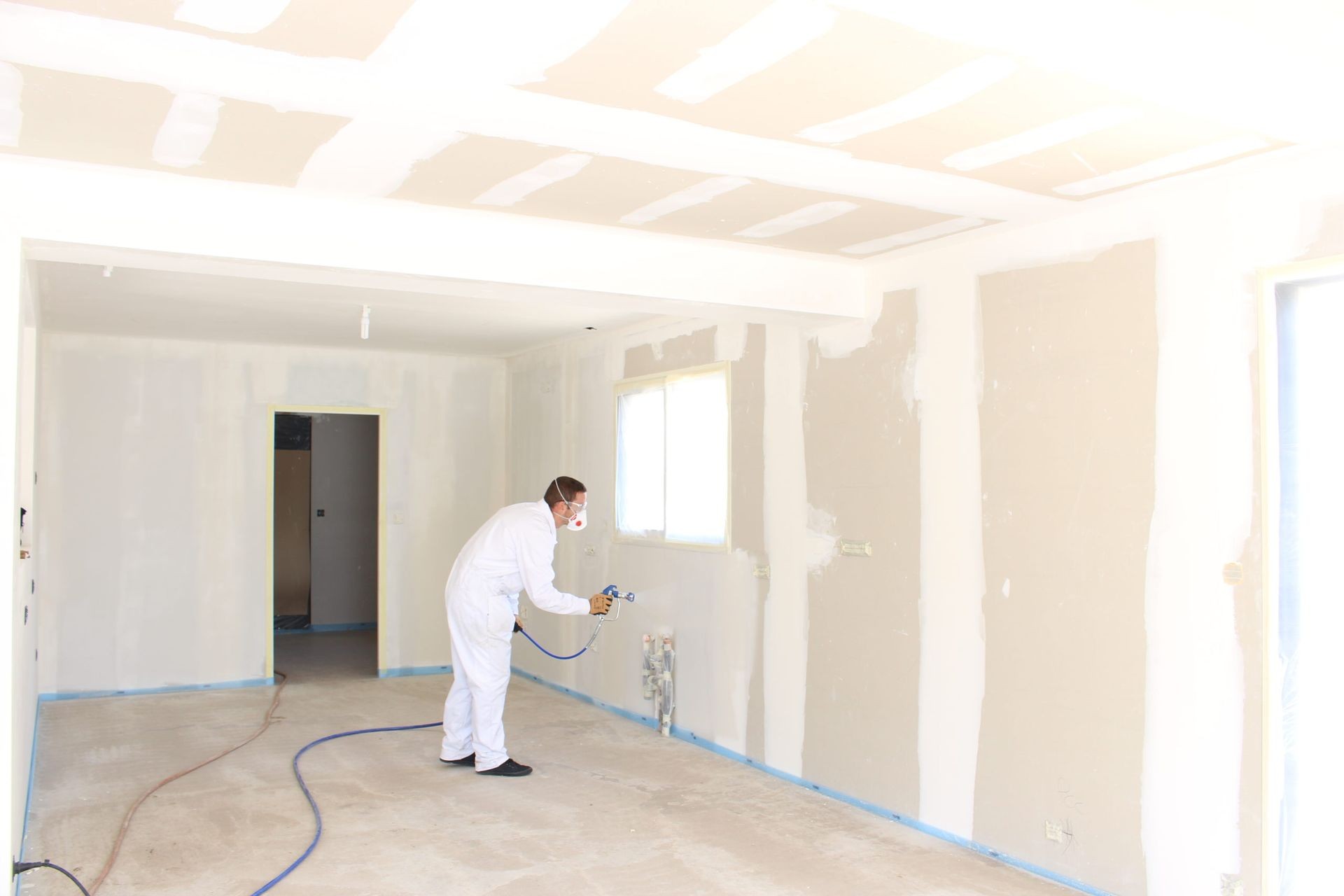 Person in white overalls spray painting interior walls of a room.